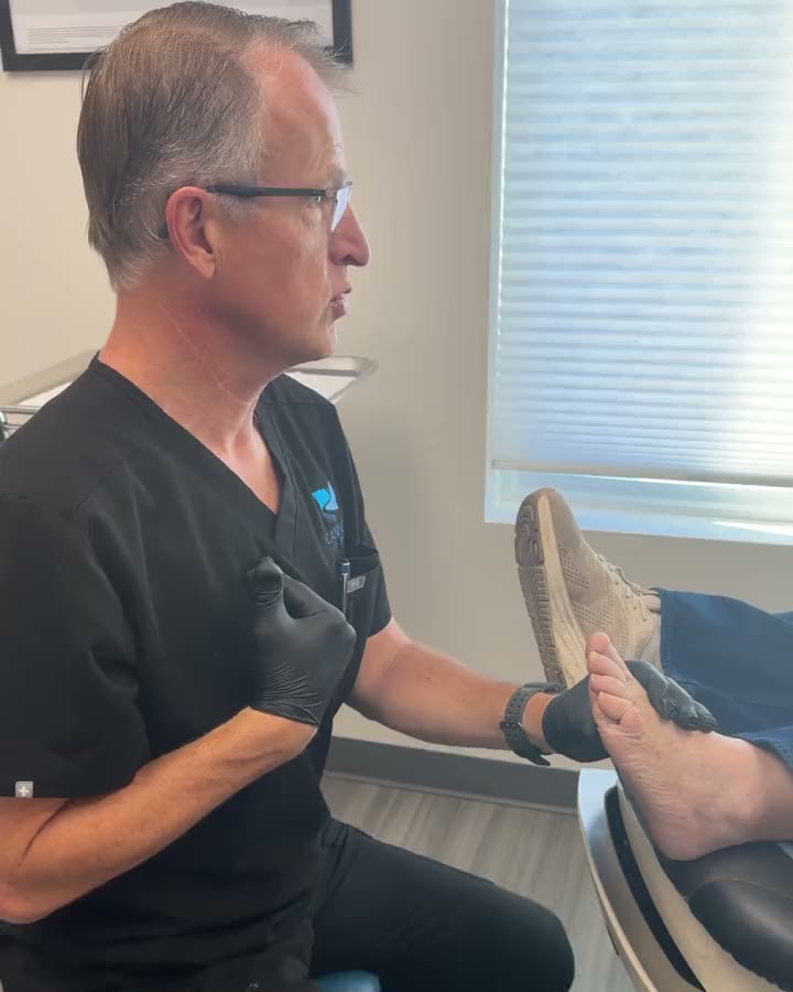 Dr. Pilling on a stool in the exam room, holding a patient's foot and talking them through their options